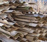 Beige and grey asbestos sheets lie in a pile.