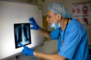 A doctor in blue scrubs looks at an X-ray in a hospital room.