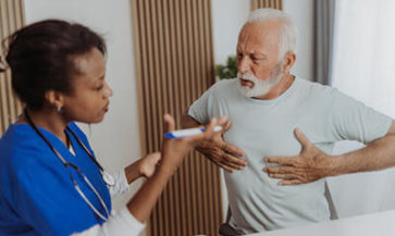 A female doctor examines an older male, who is clutching his chest to describe his symptoms.