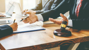 Men wearing suits sit at a brown desk. A gavel is sitting on the desk in the foreground.