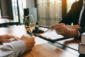 Two people sitting at a desk in a legal setting. A gavel and scales of justice are in the background sitting on the desk.