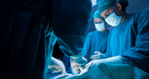 Doctors wearing blue scrubs and masks perform a surgery.