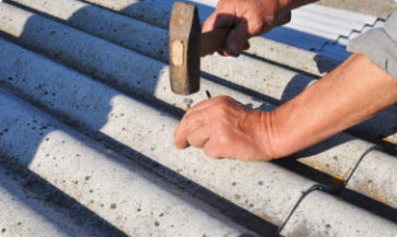 A man hammers a nail into grey asbestos sheets