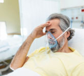 A man sits in a hospital and wears a respirator around his face.