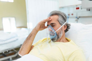 A man sits in a hospital and wears a respirator around his face.