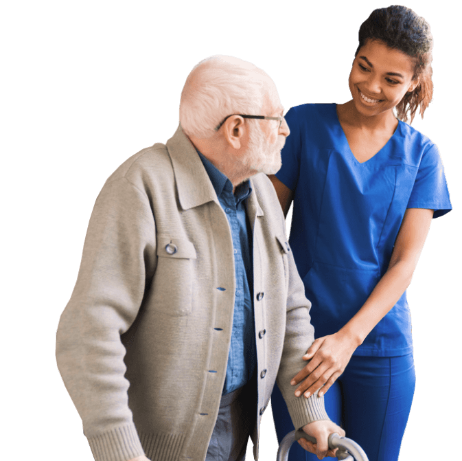 An older male walks with the help of a younger female nurse in blue scrubs.