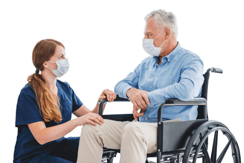A female nurse with an older man in a wheelchair. Both are wearing protective masks.