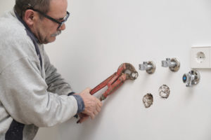 An older man works with piping on a wall.