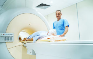 A patient gets an MRI scan in a circular machine while a doctor looks on.