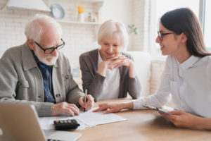 An older couple fills out documents with the help of a younger woman.