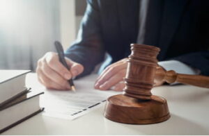 man sits at a desk filling out documents with a gavel sitting nearby
