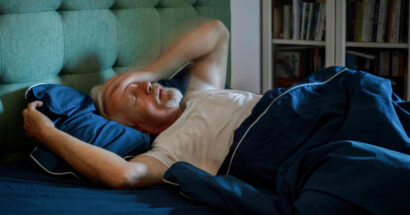 Man lying in bed with a hand across his forehead.