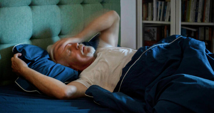 Man lying in bed with a hand across his forehead.